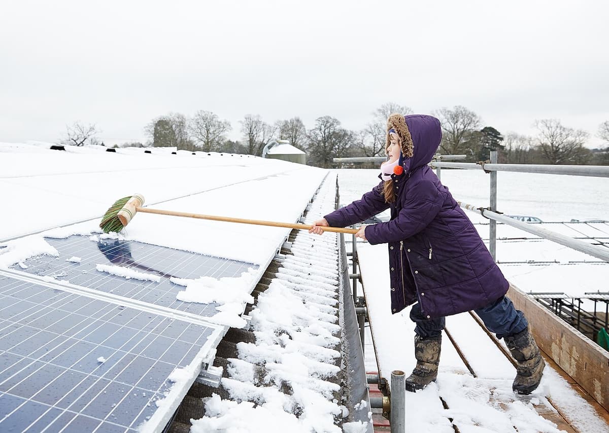Personne qui déneige des panneaux solaires avec un balai à long manche