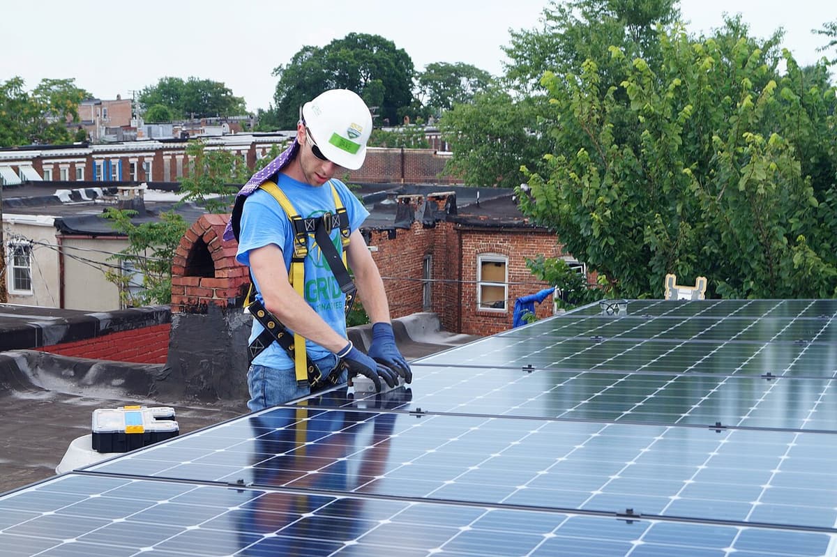 Installateur avec casque et harnais qui vérifie des panneaux solaires