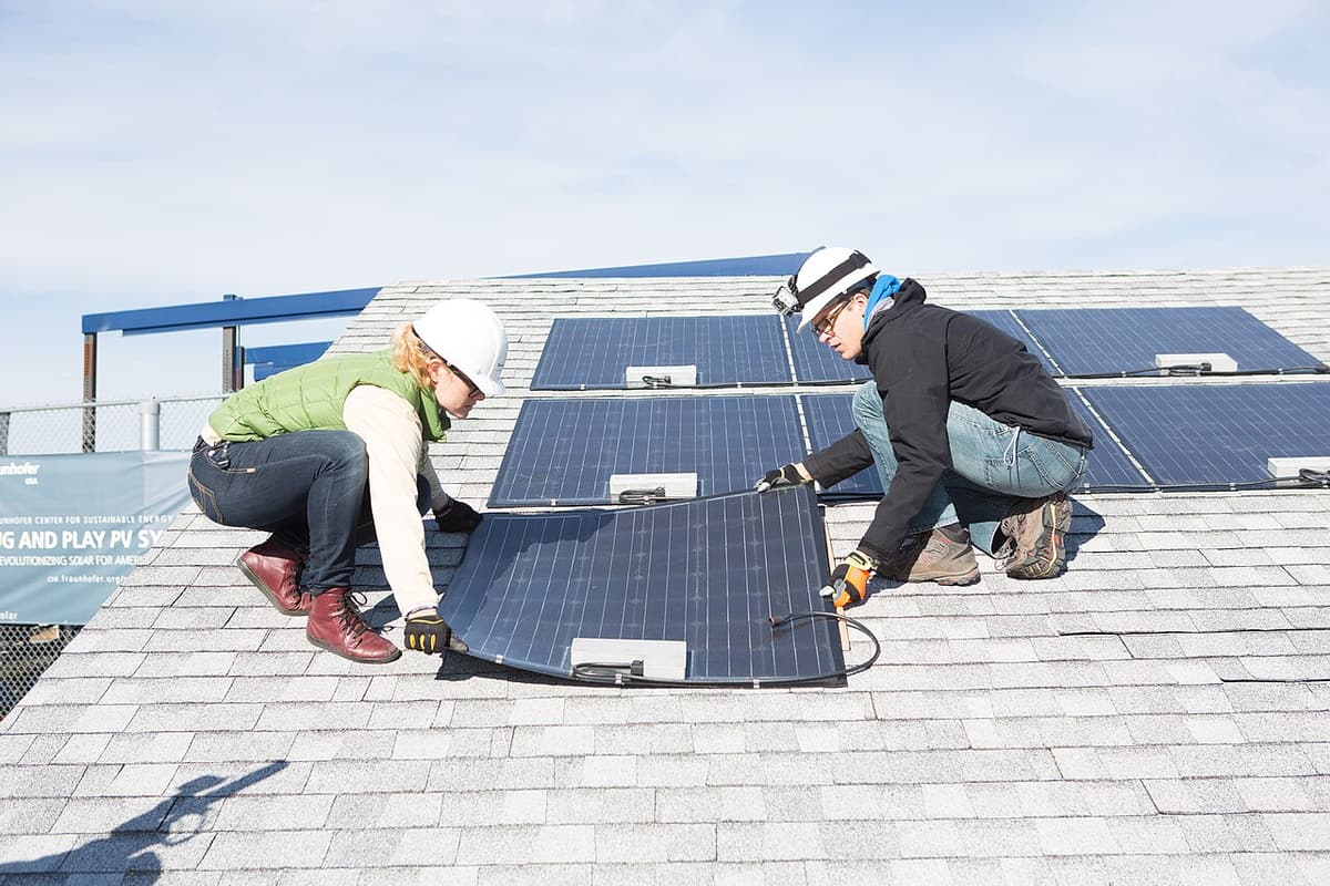 Deux installateurs avec casques posent un panneau solaire sur un toit