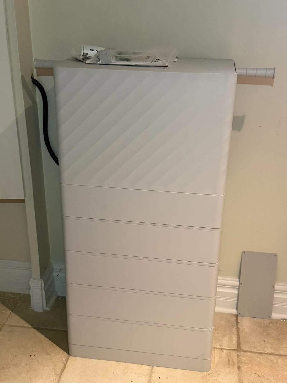 Batterie résidentielle modulaire grise installée contre le mur d'un sous-sol