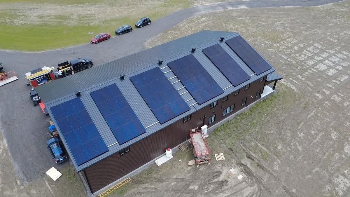 Vue aérienne d'un grand bâtiment au toit d'acier couvert de six sections de panneaux solaires