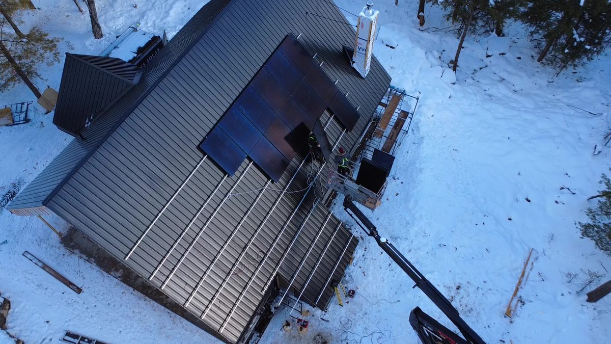 Vue de drone d'une installation en hiver : rails sur un toit d'acier, premiers panneaux posés, nacelle contre la maison, neige au sol