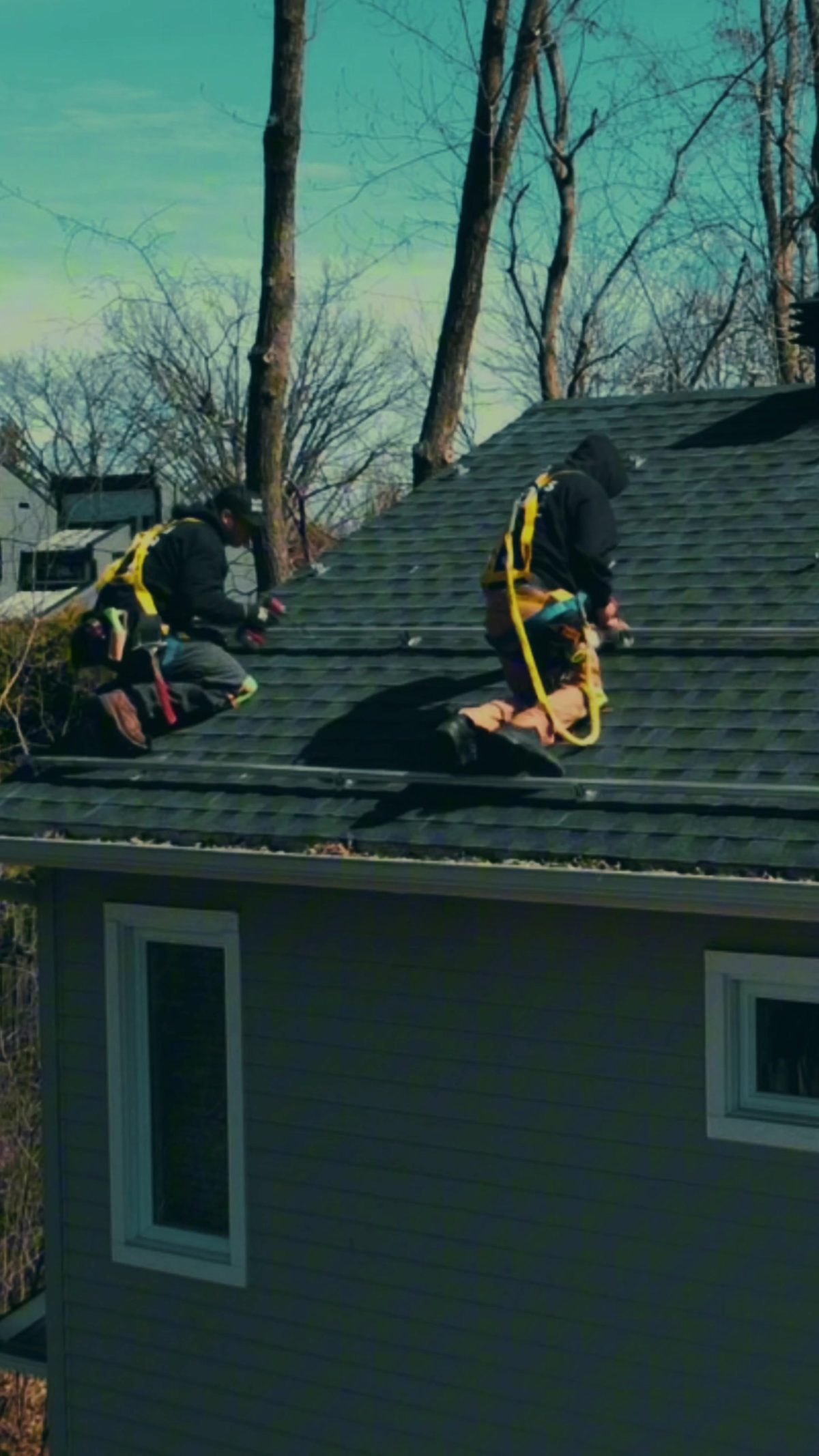 Deux installateurs de Larks Solar attachés par harnais sur un toit en bardeaux pendant la pose des rails