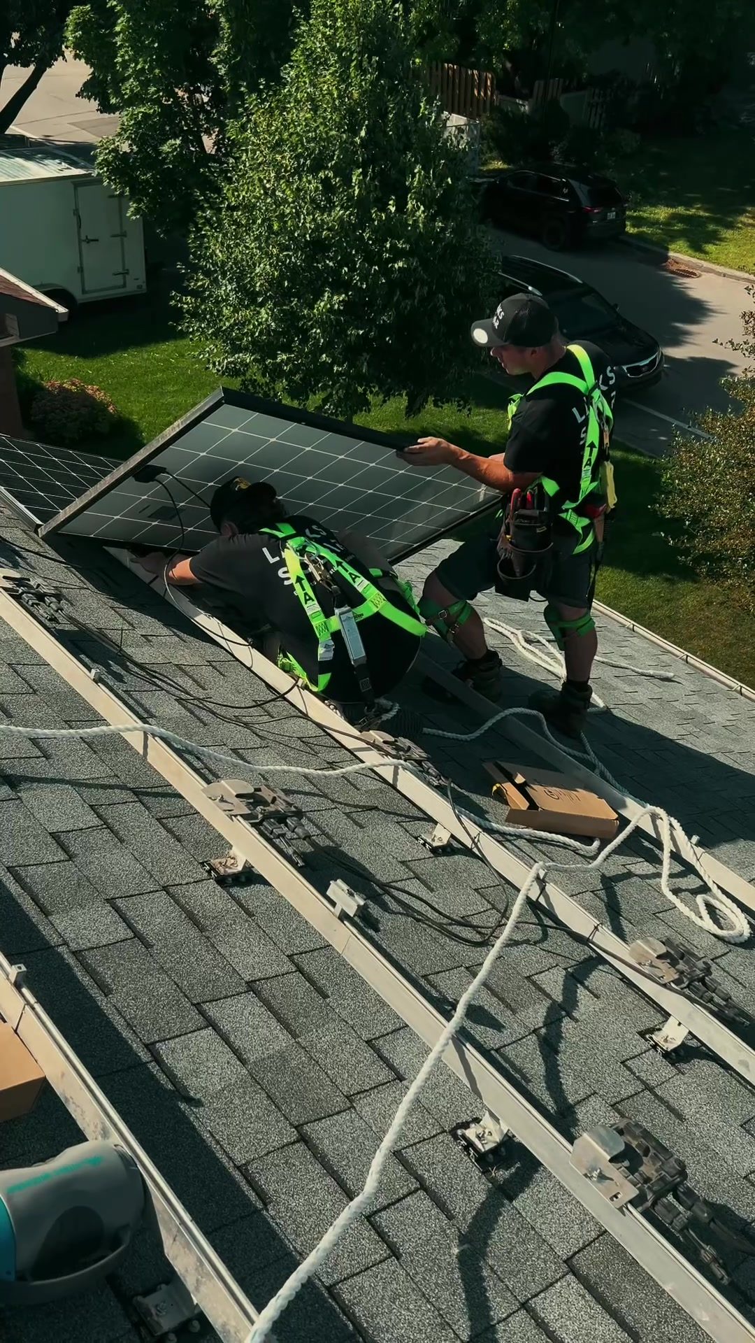 Deux installateurs de Larks Solar en dossard fixent un panneau sur des rails, toit en bardeaux