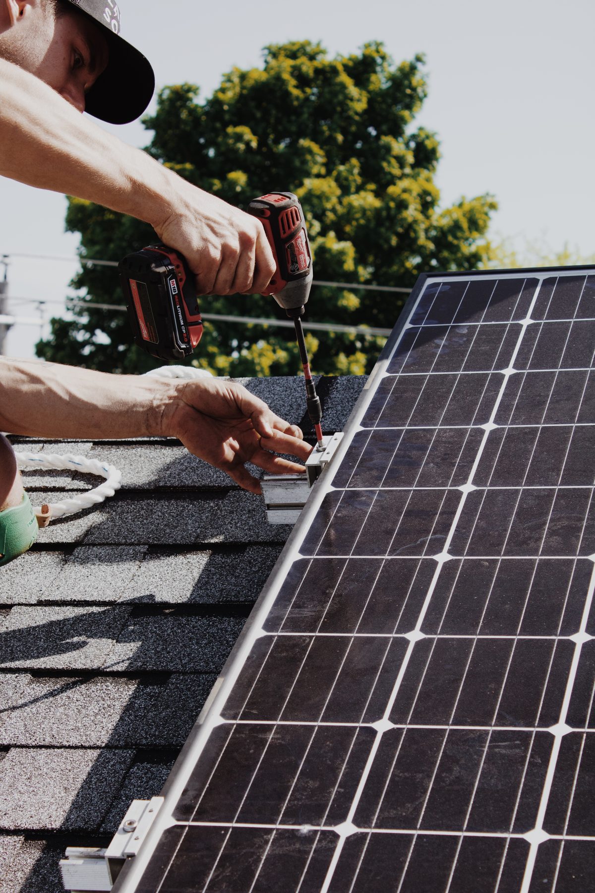 Installateur de Larks Solar, casquette Larks, qui visse une pince de panneau sur un toit en bardeaux