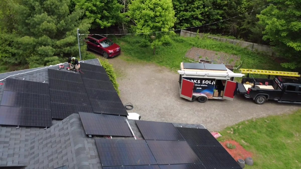 Vue de drone d'un chantier Larks Solar : panneaux noirs sur un toit en bardeaux, remorque Larks Solar et camion dans l'entrée