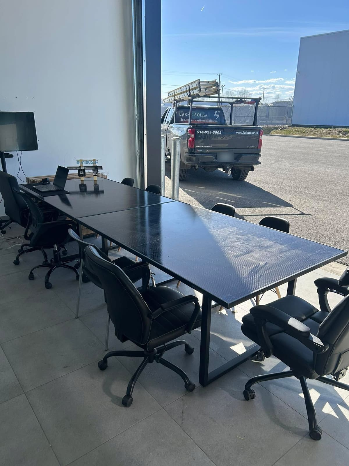 Salle de rencontre de Larks Solar à Blainville : une longue table faite de panneaux solaires, le camion Larks Solar stationné dehors