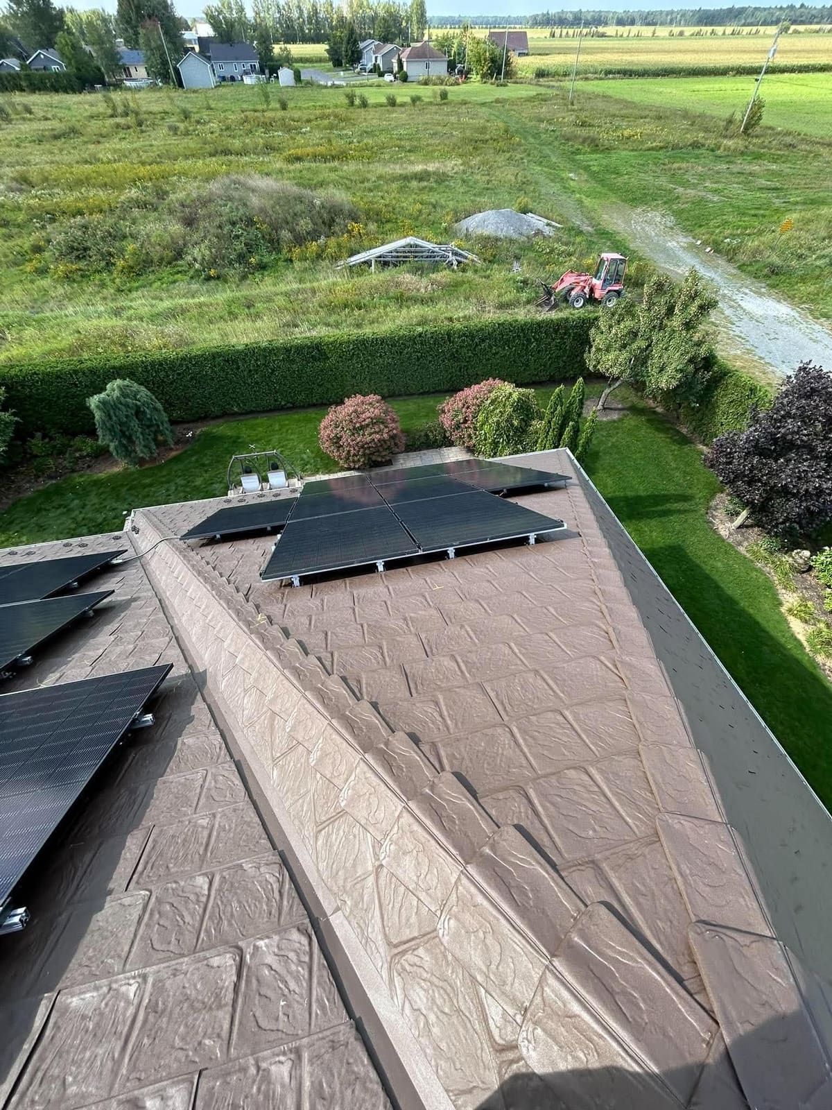 Panneaux solaires noirs sur un toit d'acier brun, vus du faîte, champs en arrière-plan